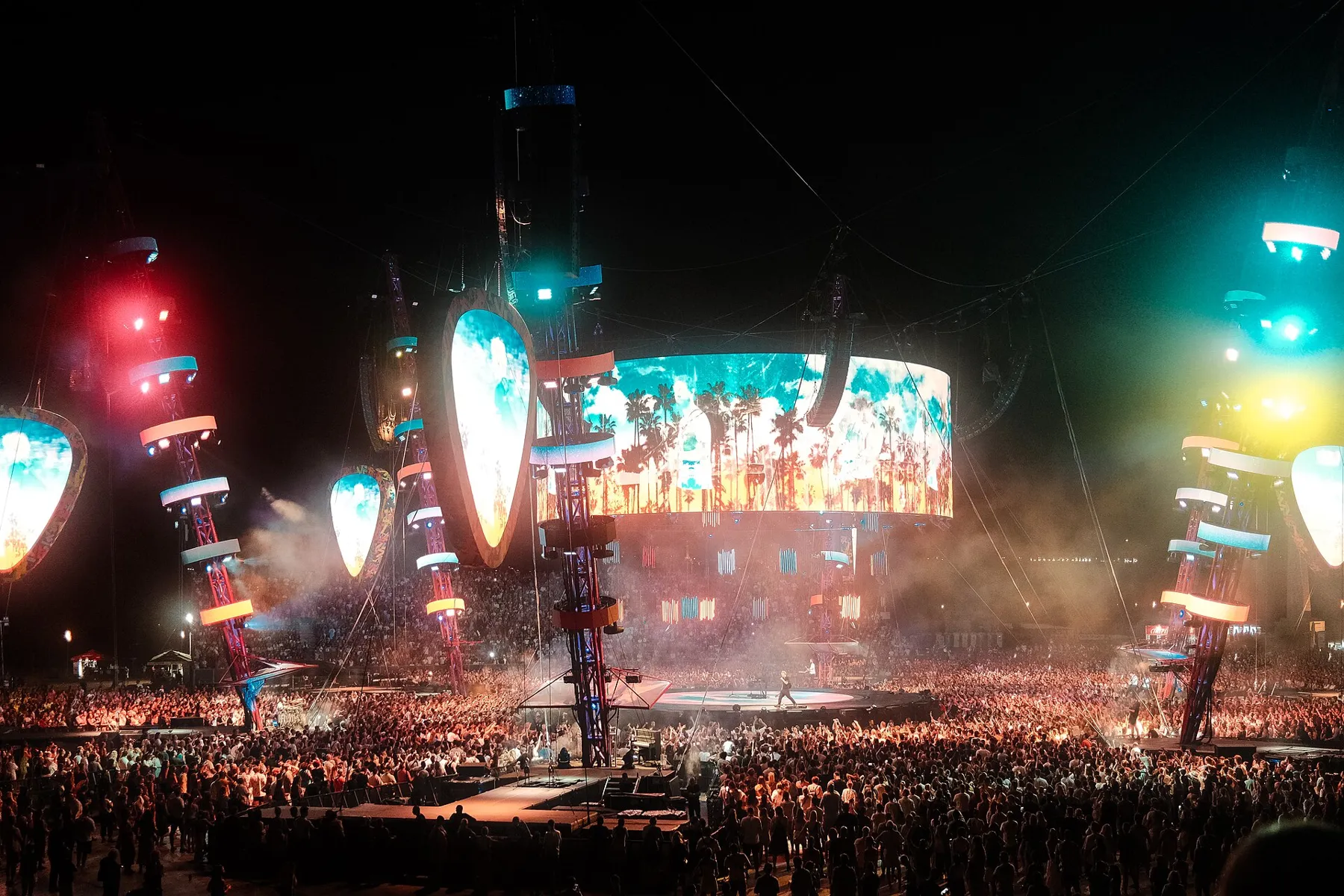 Scène de concert illuminée devant une foule, vue de loin