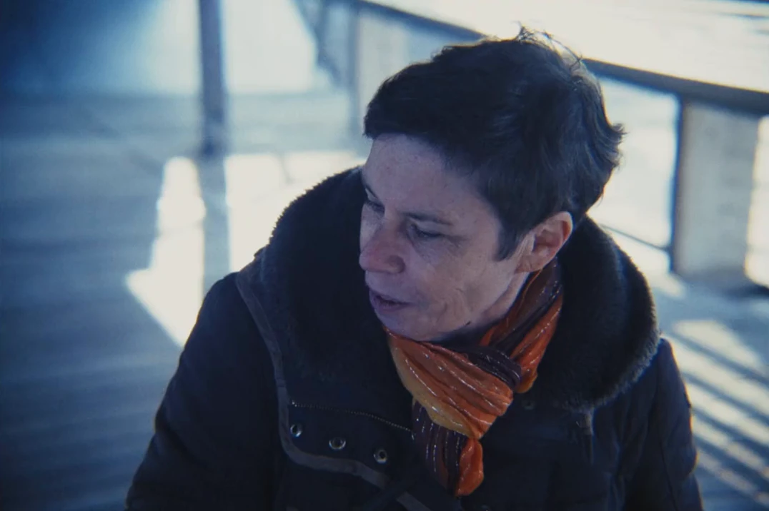 Une femme aux cheveux courts, écharpe orange, en gros plan à la fin du film, lumière froide